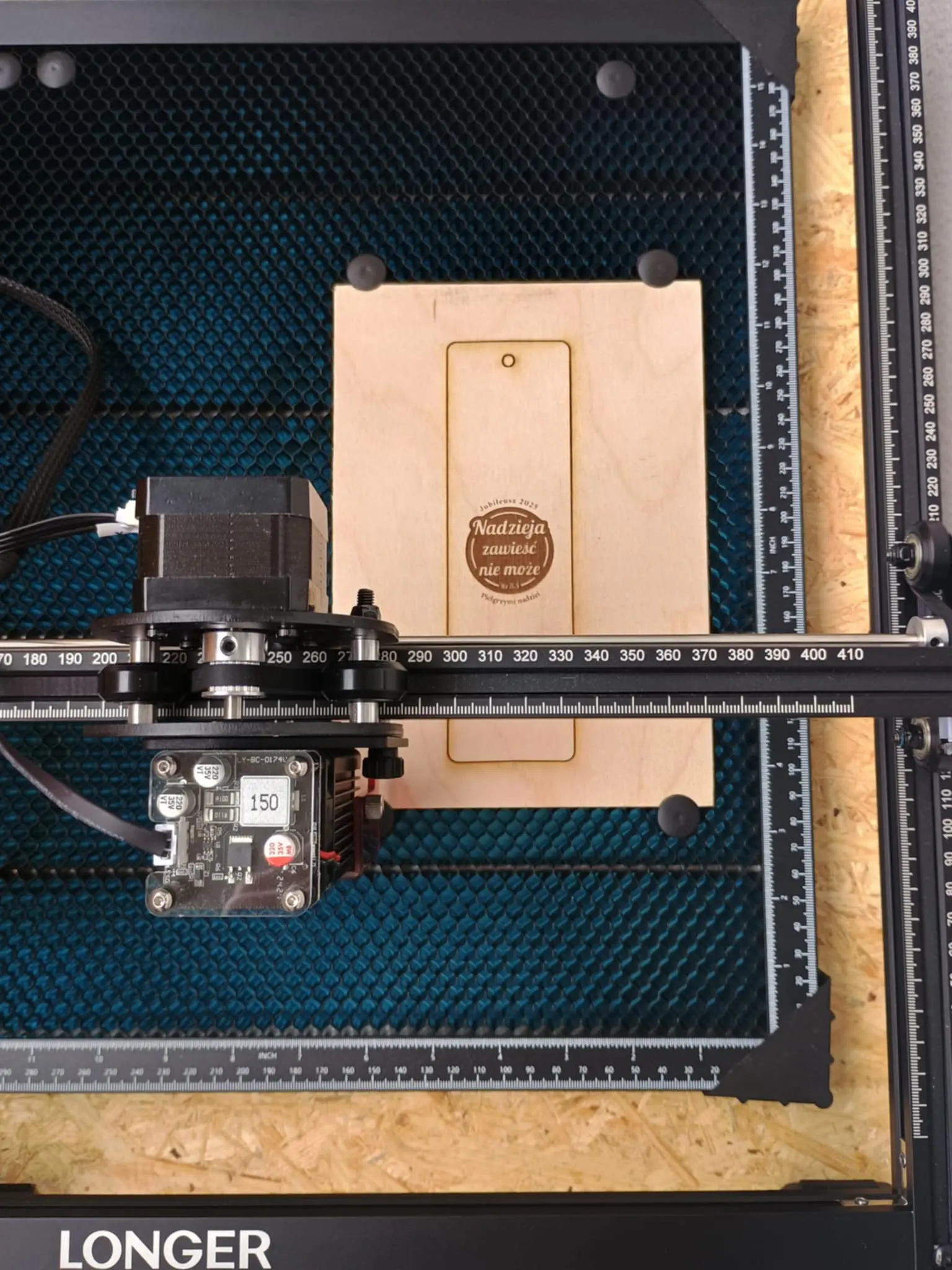 Laser i stół roboczy, na którym leży wycięta zakładka do książki z grawerem.