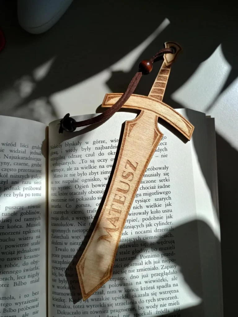 Otwarta książka z drewnianą zakładką w kształcie miecza, na której wygrawerowano imię Mateusz.